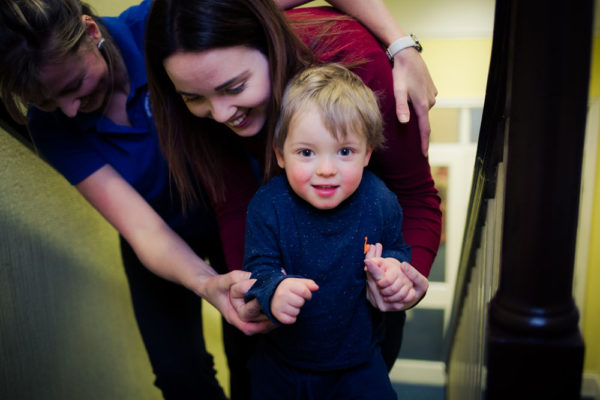 Image of child with cerebral palsy being help up by parent and charity worker